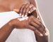 African girl in white bath towel applying body milk on her hand, free space