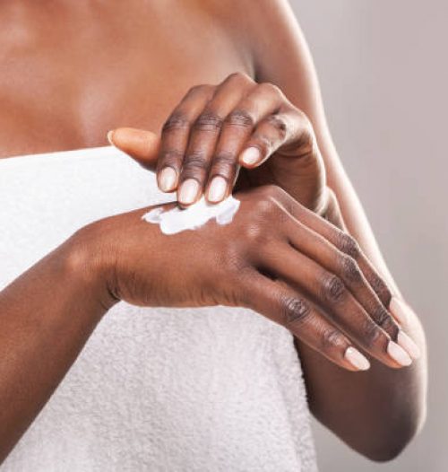 African girl in white bath towel applying body milk on her hand, free space